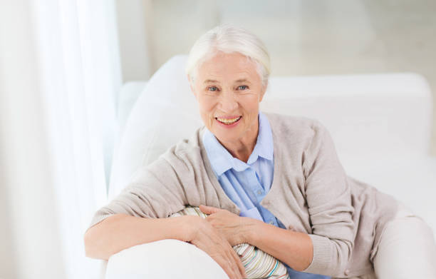 age and people concept – happy smiling senior woman sitting on sofa at home